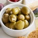 A white bowl of Belosa blue cheese stuffed green olives on a table with cheese and crackers.