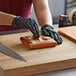 A person wearing black gloves is using a knife to cut PeachTREAT Steak Paper.