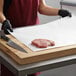 A person using a knife to cut meat on a white cutting board.