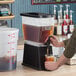 A large cold brew coffee dispenser with an 8-gallon capacity being used to pour coffee into a cup.