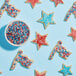 A bowl of Adourne red, white, and blue sprinkles with star shaped cookies decorated with the sprinkles.