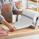 A person in a brown apron using Choice Premium Freezer Paper to wrap meat on a cutting board.