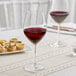 Two Acopa Bordeaux wine glasses filled with red wine on a table.