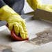 A person wearing yellow rubber gloves uses a sponge to clean a metal surface with Carbon-Off.