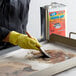 A person wearing yellow gloves using a brush to clean a dirty tray.