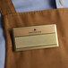 A close up of a gold rectangular Cawley nametag on a brown apron.