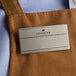 A brown apron with a Cawley silver metal rectangle name tag on it.