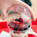 A hand holding a Dart clear plastic dome lid over a cup of fruit.