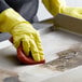 A person wearing yellow gloves using a sponge to clean a metal surface.