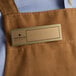 A brown apron with a gold rectangular Cawley nametag.