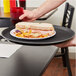 A hand holding a Carlisle black non-skid serving tray with a sandwich and a glass of red liquid.