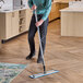 A man using a Lavex blue microfiber spray mop to clean the floor in a professional kitchen.