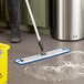 A person using a Lavex blue microfiber spray mop to clean the floor.