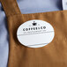 A white plastic oval nametag with black text on a brown apron.