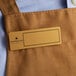 A brown apron with a rectangular gold nametag.