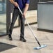 A person using a Lavex Blue Microfiber Spray Mop to clean a floor.