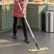 A woman using a Lavex yellow microfiber spray mop to clean the floor.