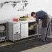 A man wearing an apron and gloves looks into an open Avantco undercounter refrigerator.