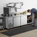 A man putting food into an Avantco stainless steel worktop refrigerator on a counter in a professional kitchen.