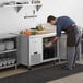 An aproned man putting food into an open Avantco undercounter refrigerator.