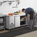 An aproned man preparing food on a stainless steel worktop refrigerator.