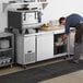 A man opening an Avantco stainless steel worktop refrigerator in a professional kitchen.