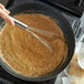 A hand using a Fox Run stainless steel flat roux whisk to stir brown liquid in a pan.