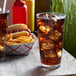 A Libbey stackable plastic mixing glass filled with cola and ice on a table with fries.