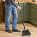 A person holding a Carlisle Sparta Duo-Sweep broom with black flagged bristles and a yellow handle sweeps the floor.