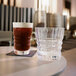 A Chef & Sommelier Cristal d'Arques highball glass filled with brown liquid and a glass of water on a table.