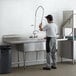 A man standing at a STEELTON sink in a commercial kitchen.