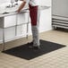 A man standing at a sink on a black anti-fatigue floor mat.