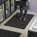 A woman standing on a black Lavex anti-fatigue floor mat in front of a refrigerator.