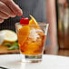 A person putting a cherry on a Libbey old fashioned glass filled with ice and a drink.