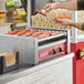 A man using an Avantco hot dog roller to cook hot dogs on a counter.