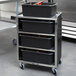 A black Lakeside utility cart with a stainless steel frame holding black bins.