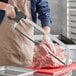 A hand using a Backyard Pro stainless steel hand meat saw to cut a piece of meat.