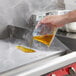 A hand pouring Noble Chemical QuikPacks Griddle Kleen liquid into a frying pan.