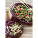 A plate of spinach salad with tomatoes and cheese on a purple Fiesta china platter.