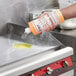 A hand pouring Noble Chemical Griddle Kleen onto a hot grill.