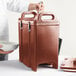 A person putting a white bowl into a brown Cambro insulated soup carrier.