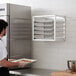 A man wearing a black apron holding a Regency sheet pan rack of cookies in front of a wall oven.