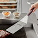 A person using a Mercer Culinary Hell's Handle® square edge turner to flip meat on a grill.