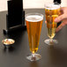 A hand holding two WNA Comet plastic Pilsner cups filled with beer.