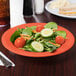 A bowl of salad with tomatoes, cucumbers, and carrots on a table with a sandwich.