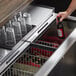 A hand holding a bottle of beer over a Beverage-Air Bottle Cooler shelf of glasses.