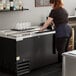 A woman standing at a refrigerated counter with a Beverage-Air black deep well bottle cooler.