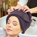 A woman getting her hair washed at a salon with a Monarch Brands eggplant hand towel over her shoulder.