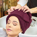 A woman with a Monarch Brands burgundy hand towel on her head getting her hair washed.