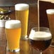 A variety of Arcoroc Linz Footed Pilsner glasses filled with different beers on a table in a brewery tasting room.